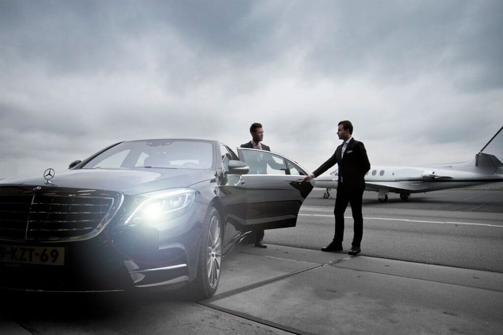 a Chauffeur opening Mercedes door and a suited person moving in the car at the apron of Boston Logan International Airport, Massachusetts